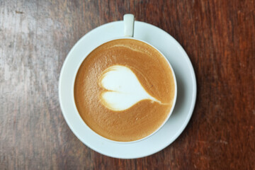 A white coffee cup with a heart drawn on it sits on a wooden table