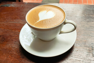 A white coffee cup with a heart drawn on it sits on a wooden table