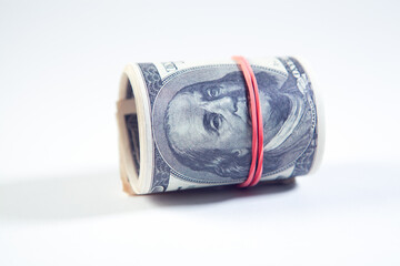 A roll of one hundred dollar bills with a red rubber band on a white background