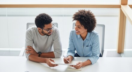 Obraz premium Two colleagues discuss work using a tablet at a bright white table.