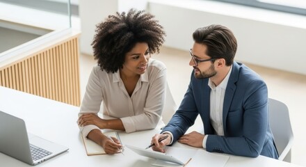 Two professionals collaborate over documents at a bright modern office table.