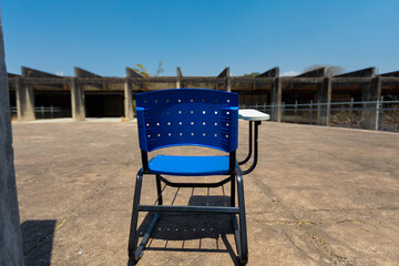 Blue plastic school chair in an abondoned place outdoors, looking into the horizon. Dropping out of school, educational crisis concept image. 