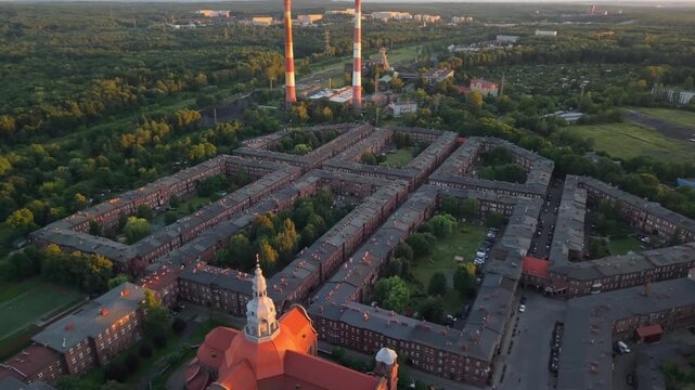Aerial drone footage of Nikiszowiec district in Katowice, Poland, during a beautiful sunset. Historic red brick buildings glowing in golden light, showcasing unique urban architecture.