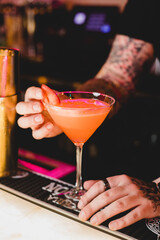 A tattooed bartender putting the finishing touches on a strawberry cocktail in a modern chic food restaurant and bar