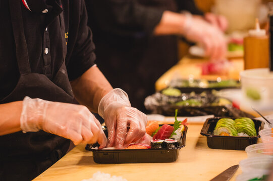 Sushi chefs wearing clear protective gloves while placing sushi in to go containers at a Japanese restaurant  - Powered by Adobe