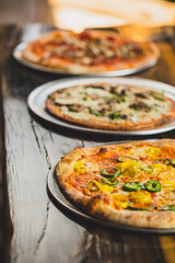 A pizza with cheese, banana peppers, and jalapeno peppers with other pizzas in the background at a bright well lit food restaurant