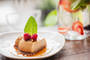 Flan served on a white plate with raspberry and mint garnishes in a brightly lit and airy restaurant