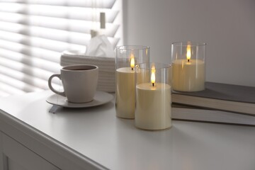 Decorative LED candles, tea, books and tissues on white table indoors