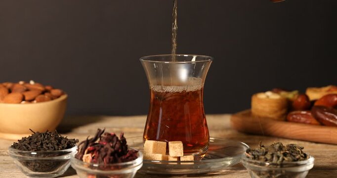 Pouring freshly brewed Turkish tea into glass at wooden table, closeup