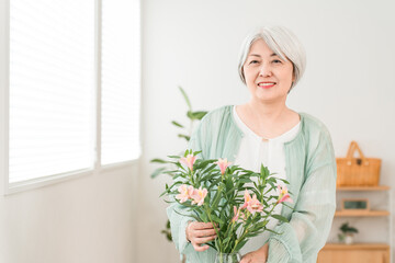 Senior woman arranging flowers in her living room (flower therapy, flower arrangement)

