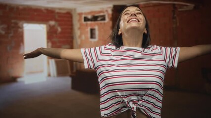 Woman with arms outstretched and head tilted back inside unfinished building under construction, smiling broadly; joy freedom renewal hope.