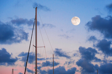 Yacht masts and the moon against the evening blue sky.