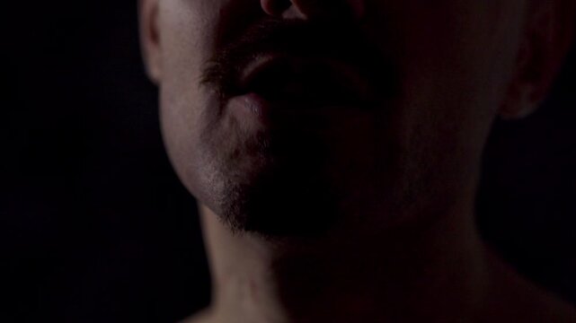 Close-up portrait of an athletic man against a dark background. He swears and points his finger at the viewer, insulting the camera man.