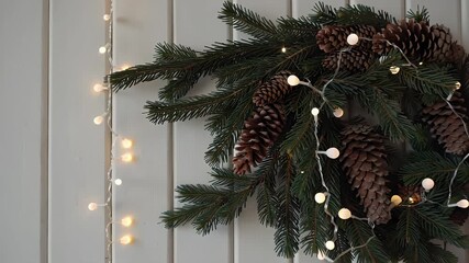 Close-up of festive evergreen branches adorned with pinecones and warm fairy lights against a wooden background - Powered by Adobe