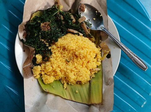 Corn rice with cassava leaf urab side dish served on a plate, rice paper and banana leaf. Traditional Indonesian food. 