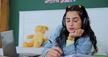 Student, laptop and girl with fidget toy for adhd, stress and writing notes on book in home bedroom. Music, headphones and woman in bed for learning, education and study for exam with sensory tangle