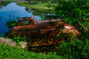 Abandoned Rusty Lifeboat or Escape Pod Submerged by the Riverside, Overgrown with Green Plants