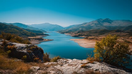 Obraz premium Expansive blue lake winds through mountainous terrain under clear sky.