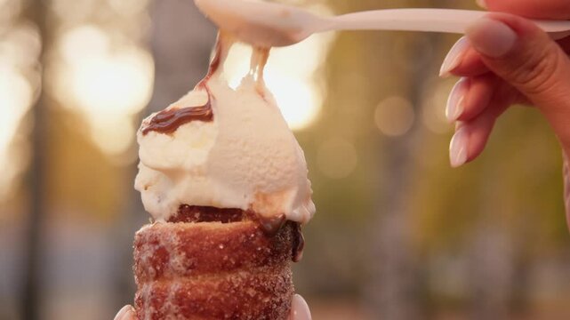 Close up of cinnamon sugar sweet and salty cone filled with creamy vanilla scoop, chocolate drizzle glistens while spoon gently adds extra sweetness.
