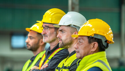 A group of construction workers wearing hard hats and safety vests are standing in a row looking at...