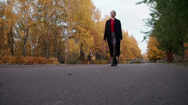 Young woman in statement footwear, black ankle boots with solid heel anchor outfit, long coat and red knit complement confident stride.