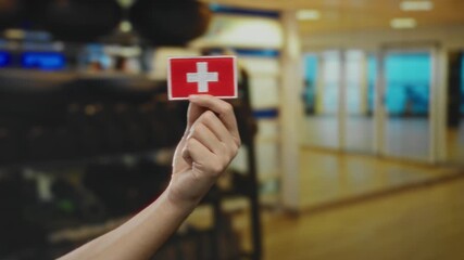 Hand of a caucasian man holding a swiss flag embroidery indoors at a sports gym with blurred background, symbolizing swiss pride and athletic spirit.