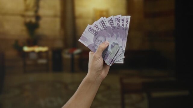 Man holding indonesian rupiah banknotes indoors, with a church background, displaying currency in a religious setting, signifying financial themes in a spiritual space.