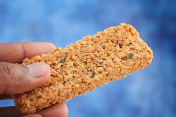 Healthy snack bar held in hand against blue backdrop