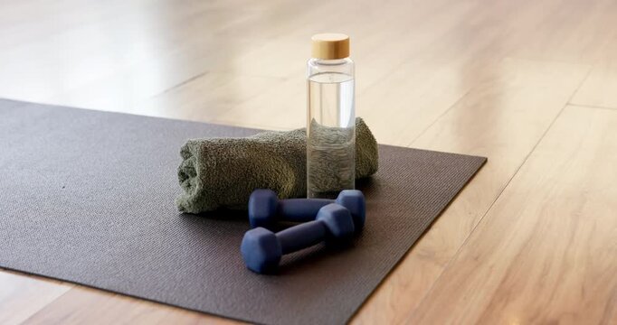 Yoga mat, dumbbells or bottle with towel in studio for fitness challenge, hydration or workout. Kneeling pad, weights or drink with cloth in gym for exercise, physical activity or liquid electrolytes