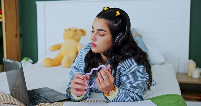 Student, laptop and girl with fidget toy for adhd, stress and reading notes on book in home bedroom. Music, headphones and woman in bed for learning, education and study for exam with sensory tangle