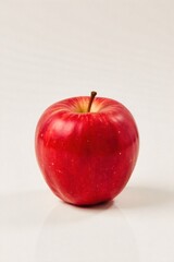 A single vibrant red apple resting on a stark white surface, casting a subtle shadow. A single, perfectly ripe red apple, studio lighting, isolated on a pure white seamless background, casting a soft,