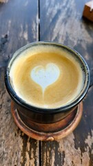 Heart-shaped latte art in a dark ceramic cup on a rustic wooden table, a warm and inviting beverage