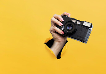 Camera film. Hand holding retro camera showing device close to camera breaking through yellow paper holes rip. Art collage digital pop modern art