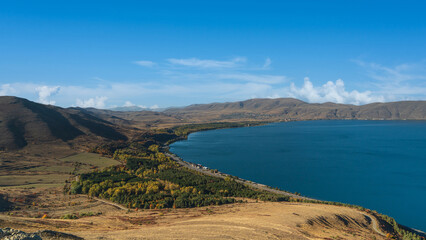 Aerial view of Lake Sevan, Armenia surrounded by dry golden hills and autumn trees. A stunning view of the lake’s shoreline and calm blue waters.