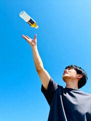 Young man throwing a bottle of drink into the air against a clear blue sky