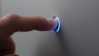 Human finger touching a chrome button glowing with blue light
