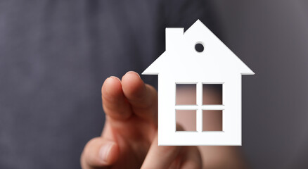 Hand reaching out to touch a symbolic house. Represents homeownership, real estate, and financial security in a digital concept.