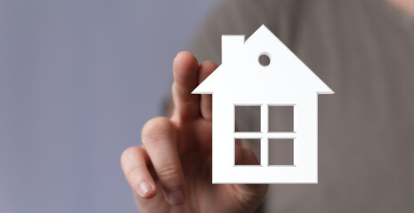 Person's hand holding a 3D house symbol, representing home ownership, real estate, and property investment. Ideal for housing, mortgage, and rea
