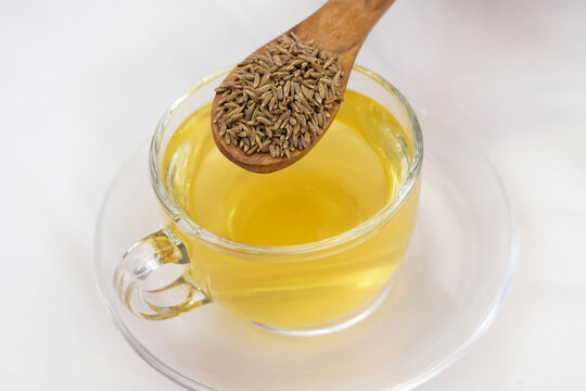 Herbal detoxifying drink isolated on white i.e. Jeera water with some raw organic cumin in a wooden spoon.