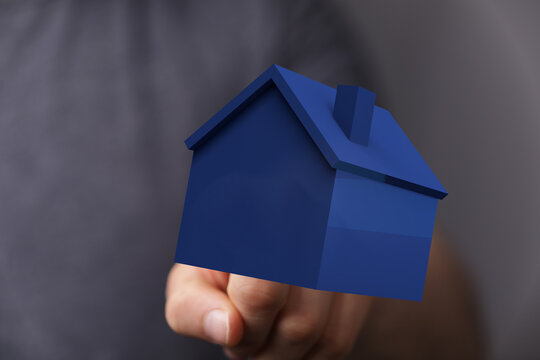 Concept of buying, selling, or owning a home. Hand holding blue house model. Ideal for real estate, mortgage, and homeownership visuals.