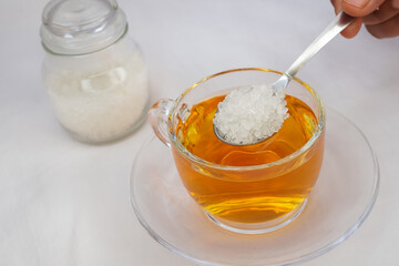 Hands of woman preparing sweet tea, holding spoon, pouring sugar powder into glass mug of hot drink, adding sweetener or fructose to beverage. Daily drink, unhealthy food concept.