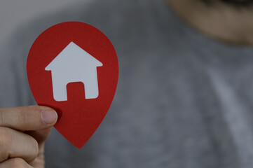 Close-up of a hand holding a red home location pin, symbolizing real estate, homeownership, and the...