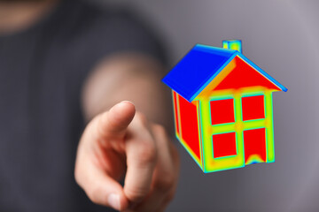A human hand pointing towards a 3D model of a house. Concept of home ownership, real estate, and property investment. Represents the idea of buy