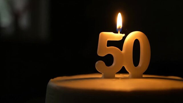 The video features a close-up of a lit '50' candle on a birthday cake, celebrating a 50th milestone in a warm, dark setting. - Powered by Adobe
