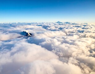A stunning aerial view presents snow-capped mountain peaks emerging from a sea of dense, white clouds under a clear, azure sky. The sun casts a warm glow