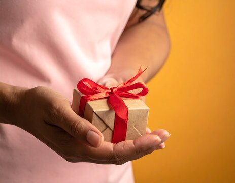 Person's hands presenting a small, wrapped gift with a red ribbon - Powered by Adobe