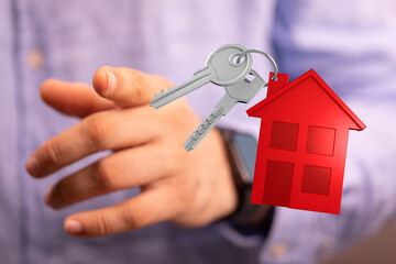Hand giving keys with red house miniature symbolizing mortgage, real estate, home buying, housing, and new home. Concept of investment and owner