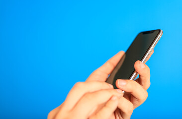 A hand holding a smartphone with a blank screen against a bright blue background. Perfect for app mockups, technology concepts, and modern commu