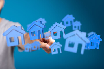 Person's hand reaching towards blue house icons representing home ownership, mortgages, and property. A concept for buying or selling real estat
