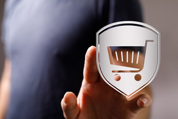 A person's hand interacting with a shield icon displaying an online shopping cart, symbolizing...
